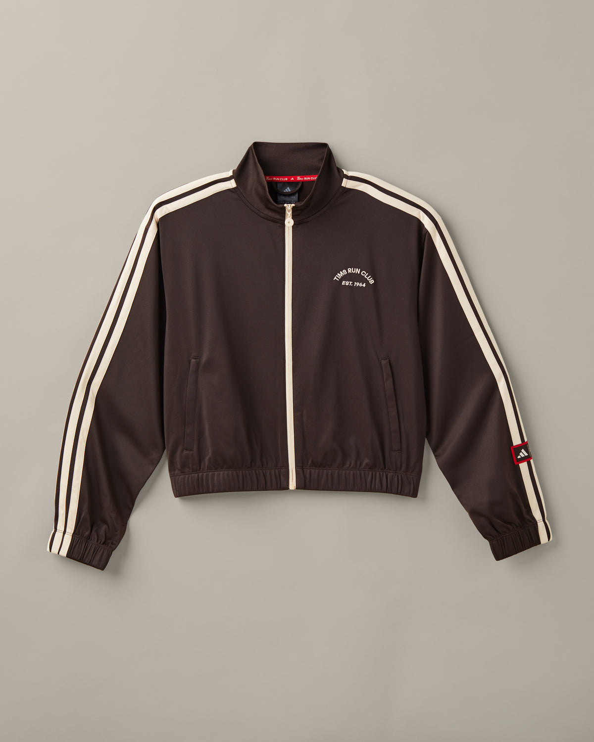Women’s cropped espresso-brown adidas® track top with a cream zipper, cream 3-Stripes, and a Tims Run Club chest graphic. - Image #1