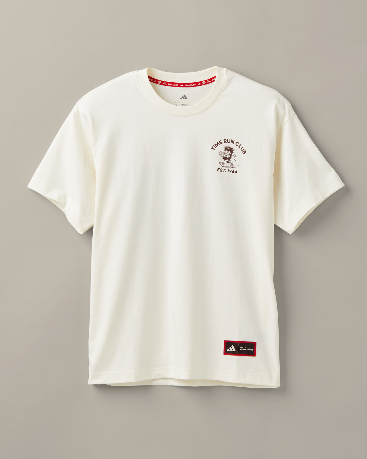 Cream unisex T-shirt featuring coffee-and-donut characters running past a classic Tim Hortons restaurant. - Image #1