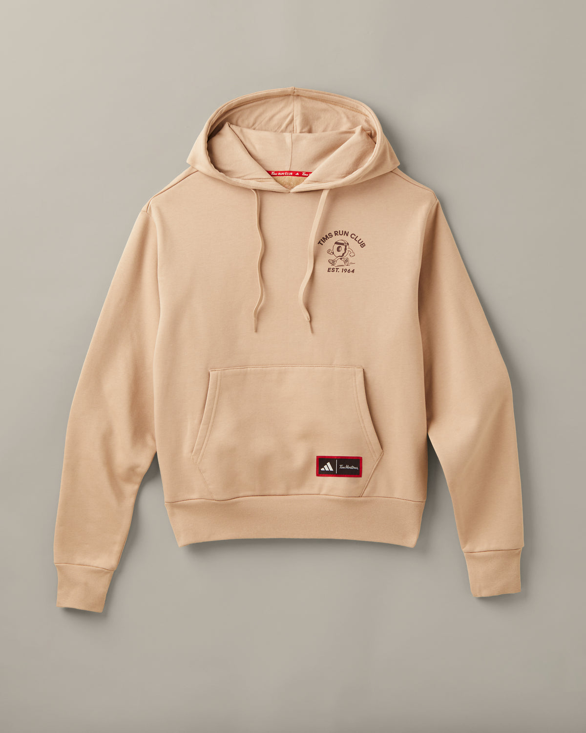 Cream adidas® pullover hoodie with a Tims Run Club donut character on the chest, kangaroo pocket, and co-branded patch. - Image #1