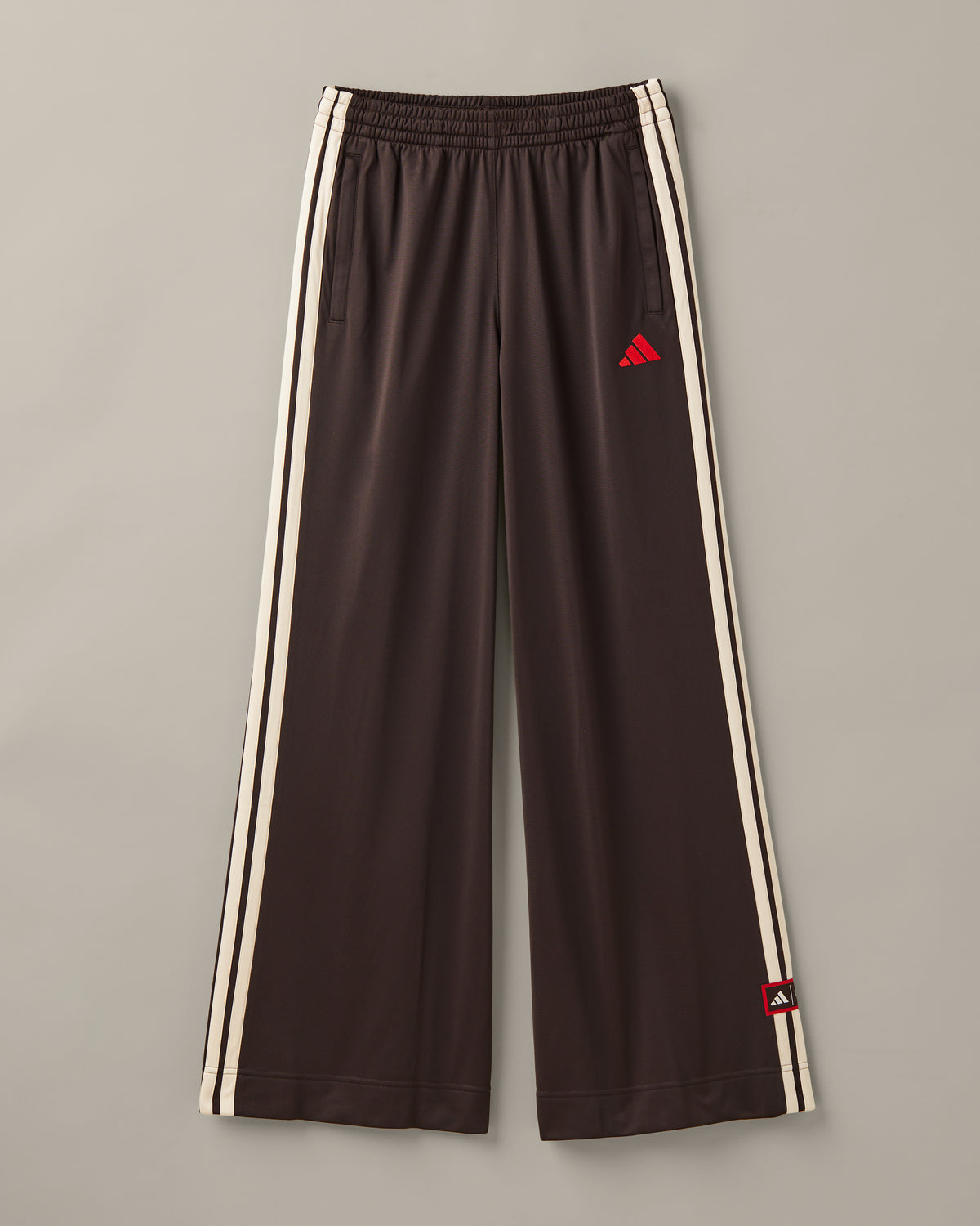 Women’s wide-leg espresso-brown adidas® track pants with cream 3-Stripes and red co-branded details. - Image #1