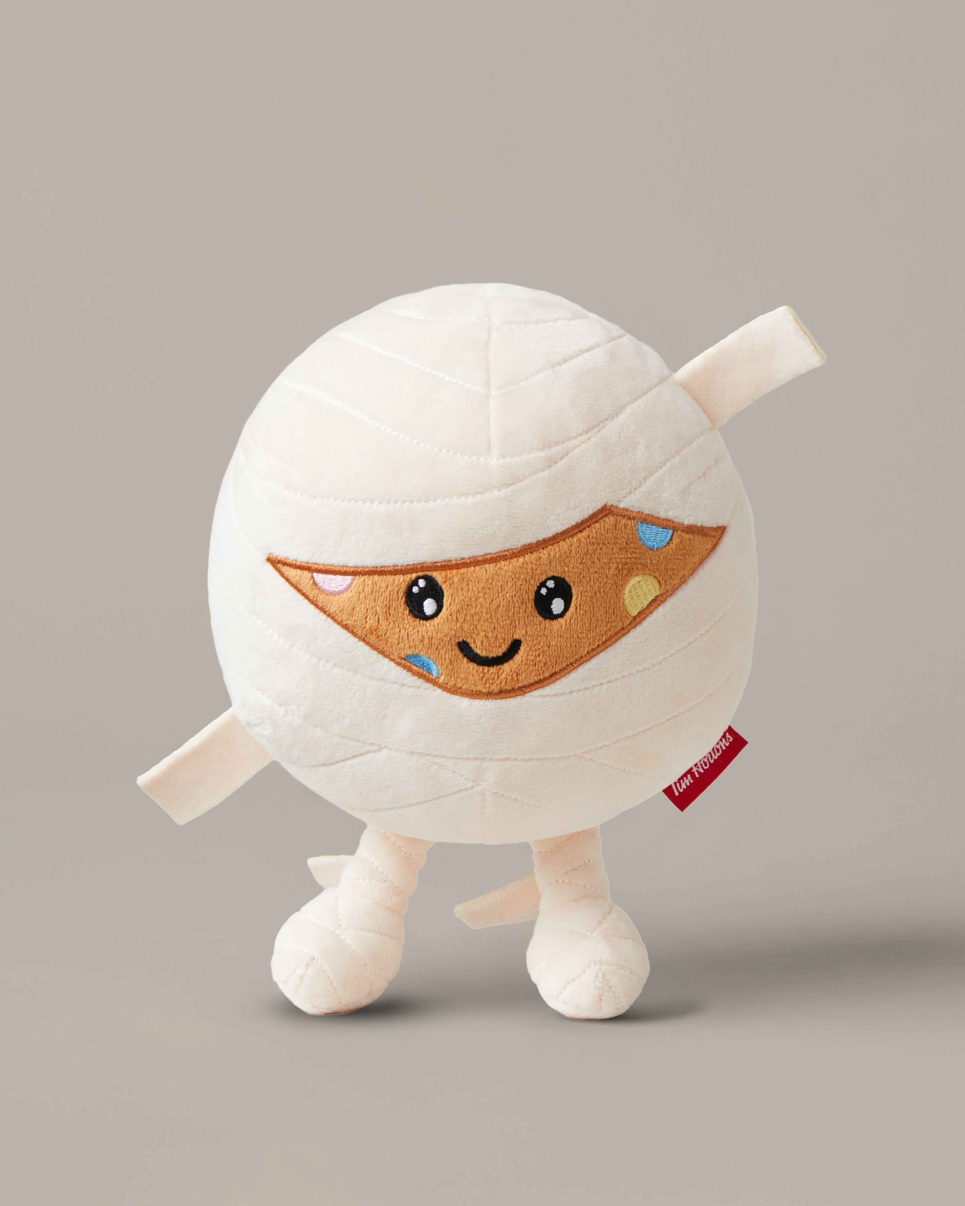 Timbits® Mummy plush with white wrapping, an embroidered face and black-and-white striped legs. | Peluche momie TimbitsMD avec bandelettes blanches, visage brodé et jambes rayées noir et blanc. - Image #1