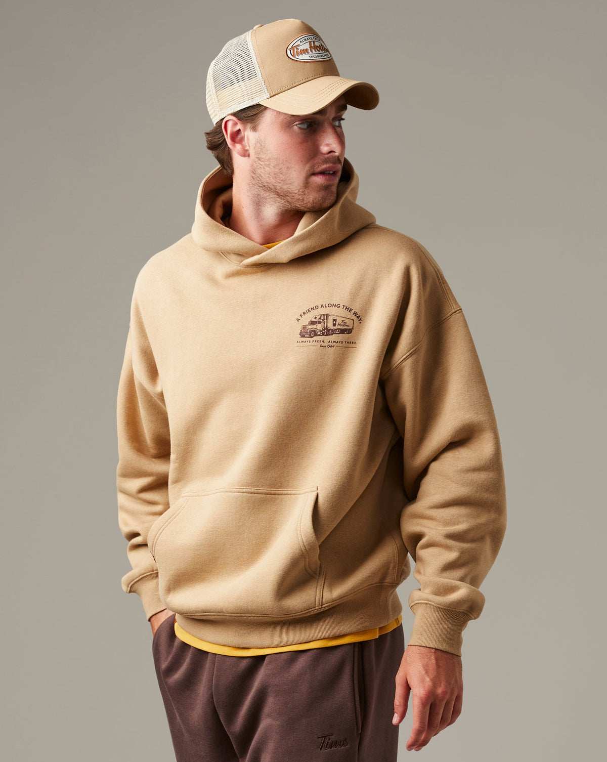 Beige Tim Hortons pullover hoodie with a kangaroo pocket and small A Friend Along the Way delivery truck graphic on the chest. | Chandail à capuchon Tim Hortons beige avec poche kangourou et petite illustration de camion de livraison « Un ami sur la route » sur la poitrine. - Image #3